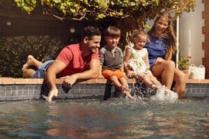 family playing by pool testing out ideal pool temperature